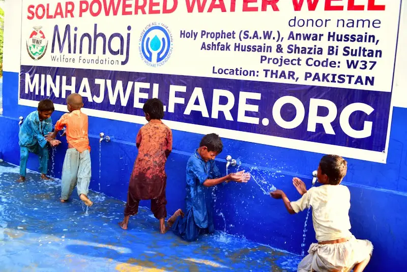 Minhaj Welfare Foundation solar-powered water well in Thar, Pakistan, with children enjoying clean water, supported by Sindh Development Organization (SDO) NGO