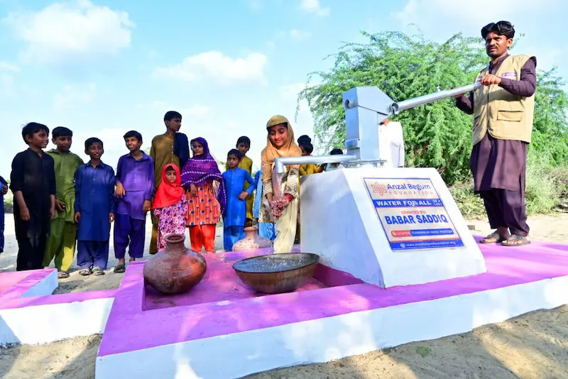 Water for All project by Anzal Begum Foundation with help of SDO in Tharparkar, Sindh, Pakistan, with a man operating a pump and children gathering, supported by Babar Sadiq