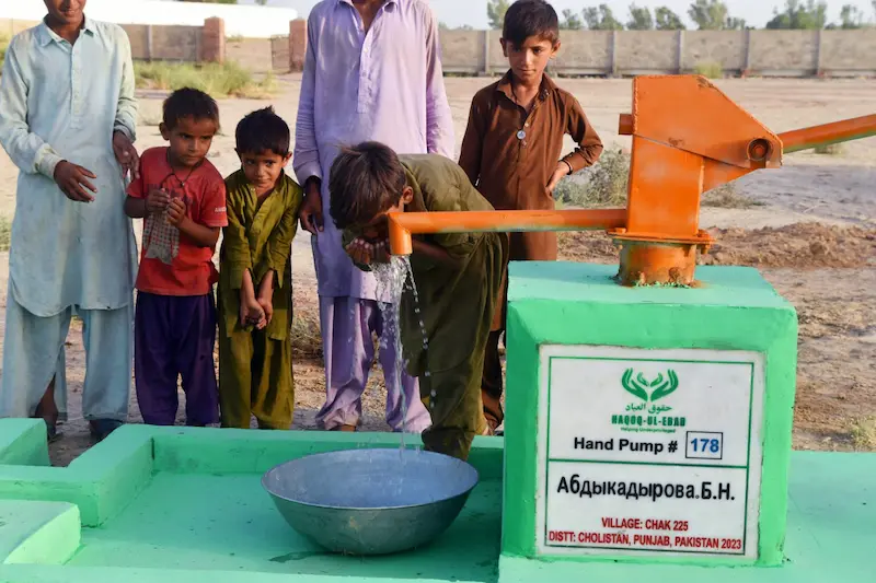Kids and adults using a hand pump by Sindh Development Organization (SDO) NGO in Chak 225, Punjab, Pakistan, for clean water, supporting health, dated 2023.