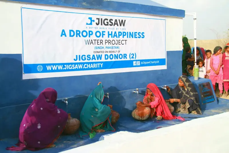 Jigsaw Charity's "A Drop of Happiness" water project in Sindh, Pakistan, with women filling pots at taps, supported by anonymous donors