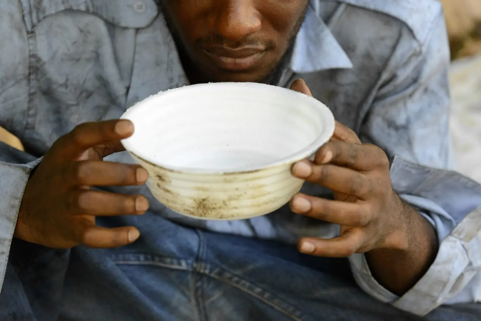 Person holding an empty bowl, symbolizing hunger and need for food aid, highlighting poverty and humanitarian support in underprivileged communities
